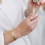 Close-up of a wrist wearing four gold bracelets holding a gold lipstick with a blurred background