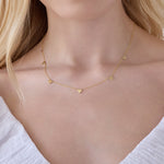 Close up of a  woman's neck wearing a 5 of Hearts Necklace in yellow gold with a white top and her blonde hair partially visible. 