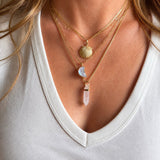 Close-up of a person wearing multiple gold necklaces with pendant stones on a white background