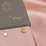 Charm Studs - Moon and Star in yellow gold in a Maya Brenner jewellery box against a light pink silk background.