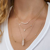 A close-up of a woman’s neck wearing four yellow gold necklaces: two Custom Gold Necklaces (one with three charms and the other with four charms), the Clarity Retreat Necklace and the Diamond Arc Layering Necklace, with a white top.