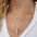 A close-up of a woman’s neck wearing four yellow gold necklaces: two Custom Gold Necklaces (one with three charms and the other with four charms), the Clarity Retreat Necklace and the Diamond Arc Layering Necklace, with a white top.