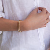 A close-up of a woman's arm and hand wearing two Classic Bubble Bracelets, two Delicate Beaded Bands and a Twinkle Twinkle Ring, with a white shirt. 