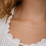 Close-up of a person wearing a delicate gold necklace with a cross pendant, against a neutral background.