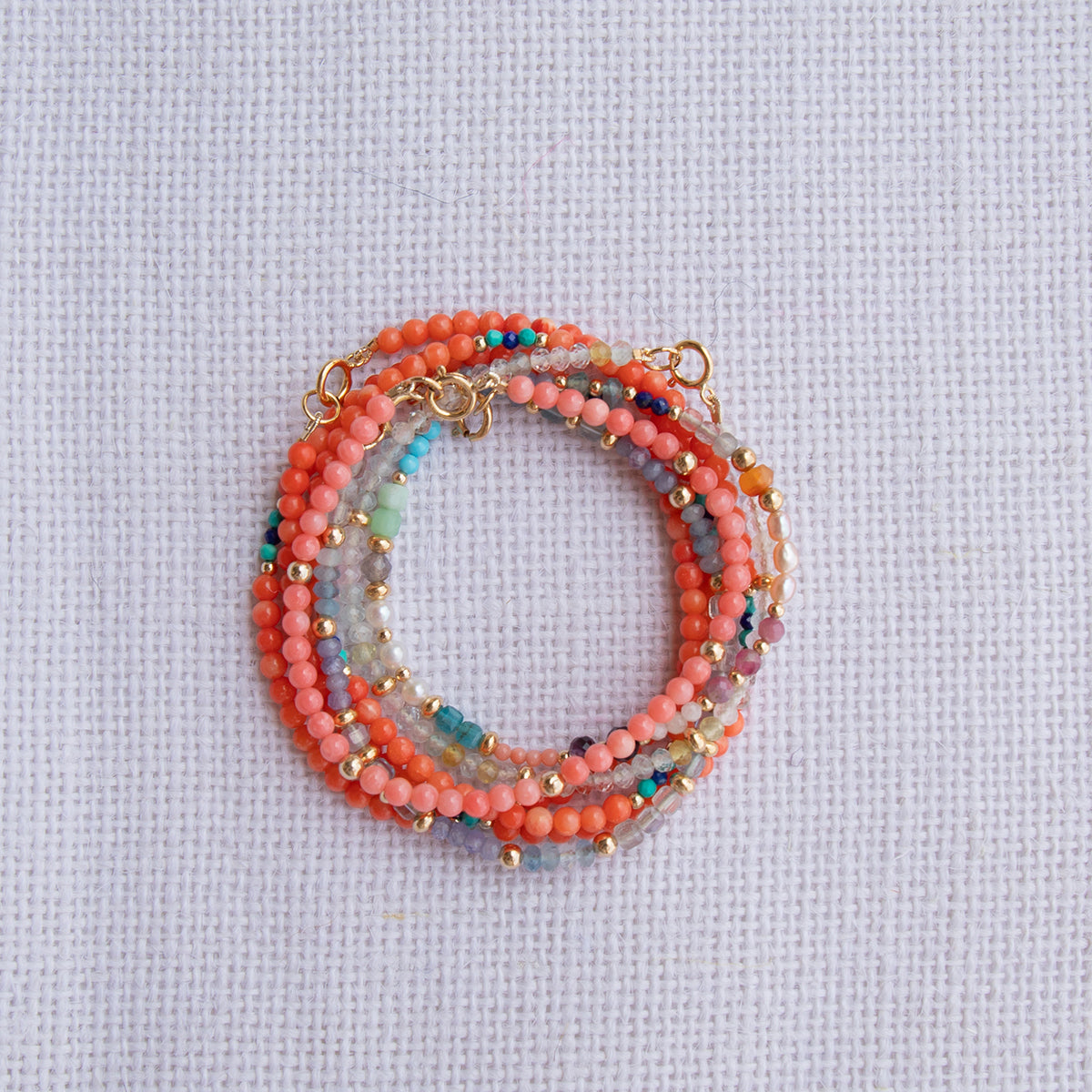 Several Endless Summer Bracelets stacked on a white fabric background. 