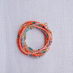 Several Endless Summer Bracelets stacked on a white fabric background. 
