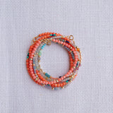Several Endless Summer Bracelets stacked on a white fabric background. 