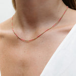 A close-up of a neck wearing a Confetti Necklace - Pink, styled in a white top. 