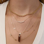 Close-up of a person wearing multiple gold necklaces with various pendants on a neutral background.