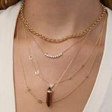 Close-up of a person wearing multiple gold necklaces with various pendants on a neutral background.