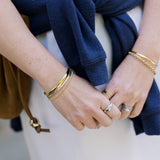 Close-up of hands with gold bracelets and rings, wearing a blue sweater.