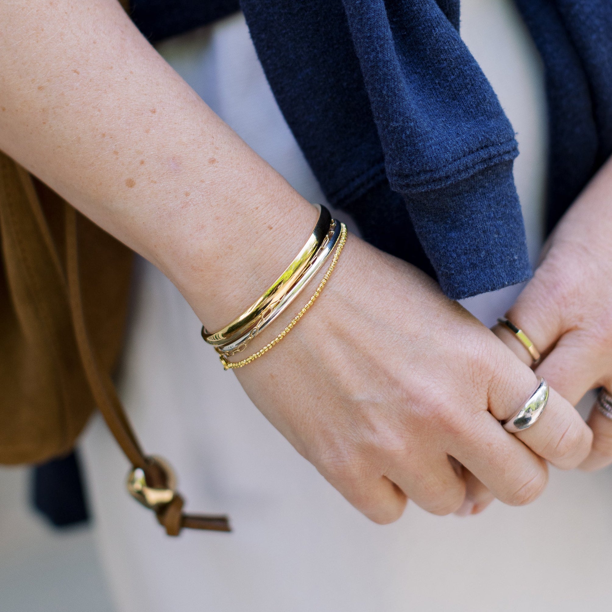 Close-up of hands with gold bracelets and rings, wearing a blue sweater.