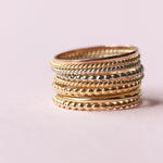 Several Delicate Trio Stacking Rings in yellow gold and white gold on a light pink background. 