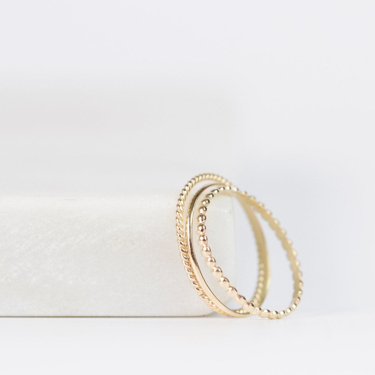 Delicate Trio Stacking Rings in yellow gold on a white surface and background. 