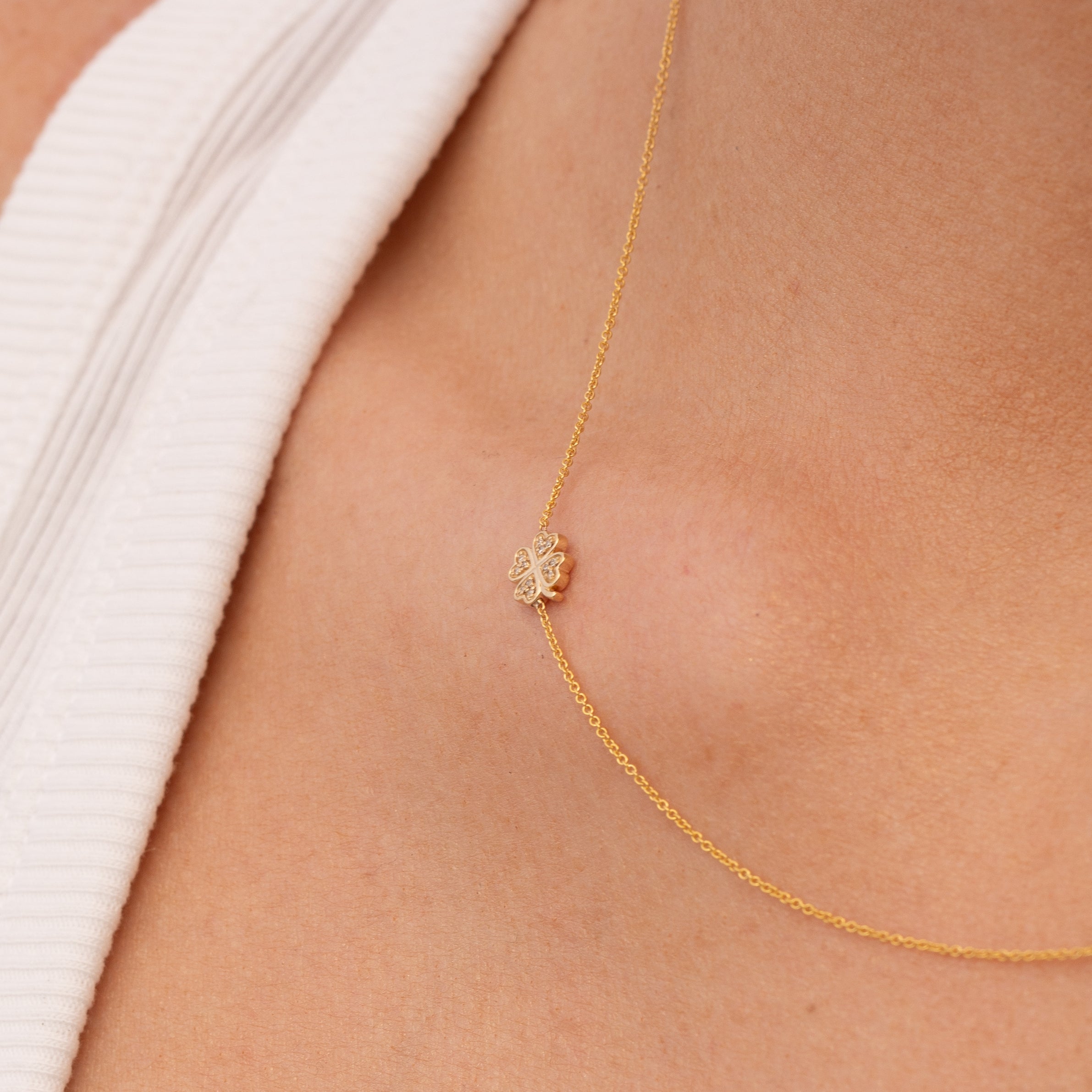 Gold chain with a diamond clover charm on a person's skin