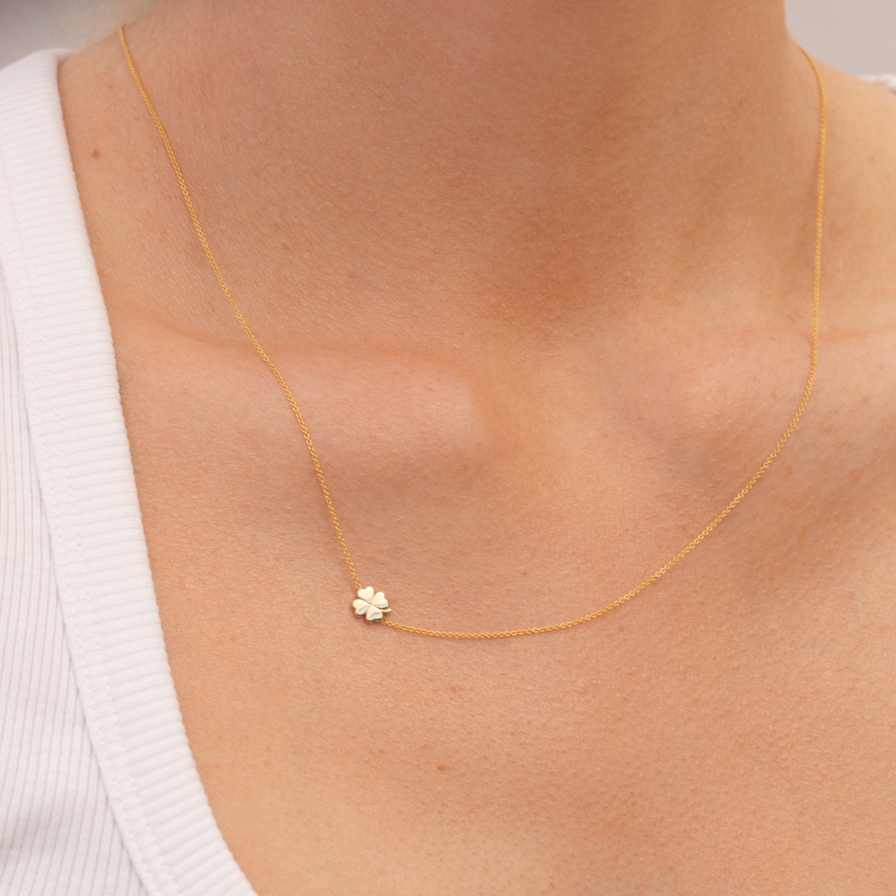Gold necklace with a small four leaf clover charm on a person wearing a white tank top.