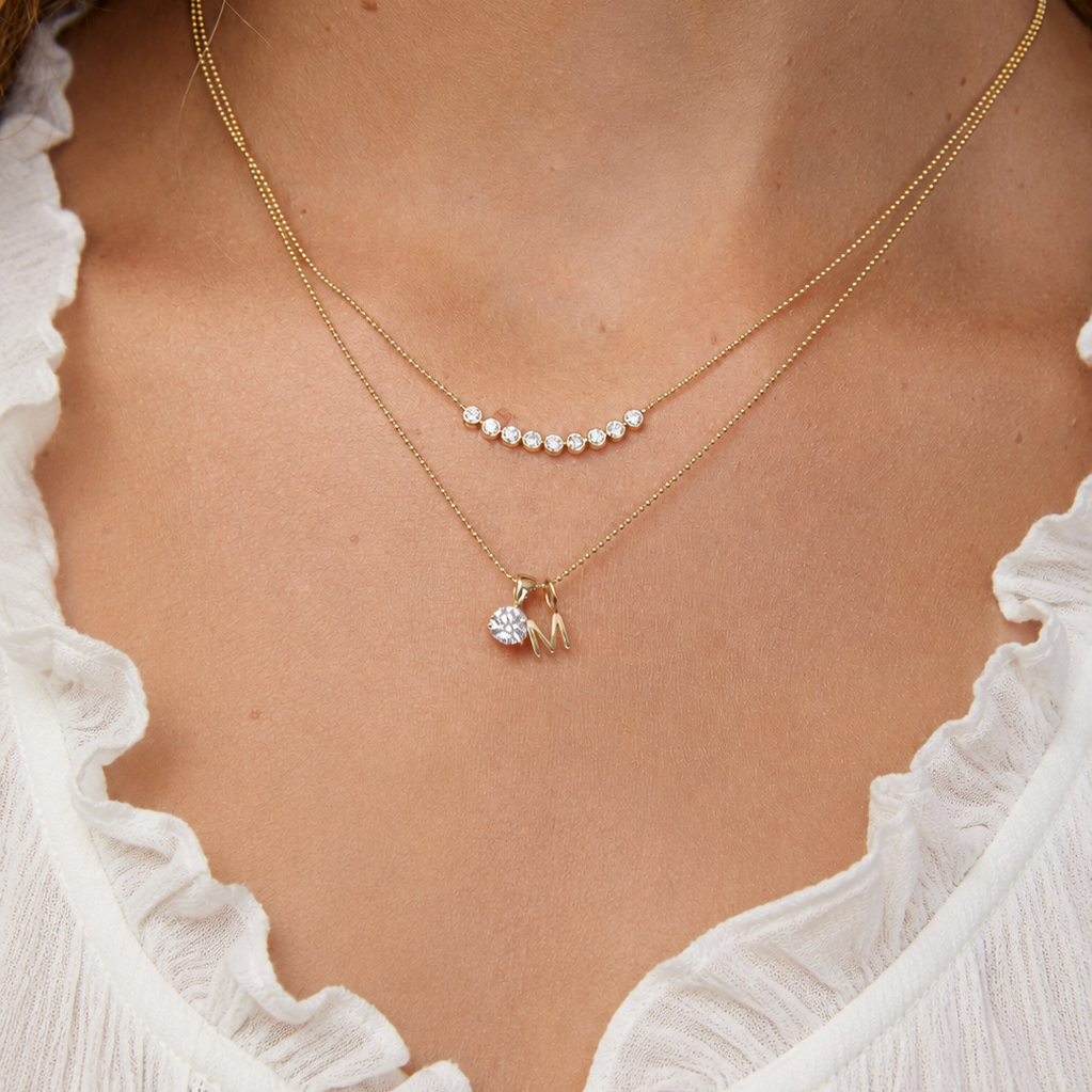 Diamond Arc Layering necklace with a Gold Letter Jumble Necklace on a person wearing a white top