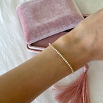 An arm wearing a Tie-Breaker Bracelet with a velvet pink box and tassle in the background. 