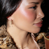 Close-up of a woman wearing a Highball Diamond Chain Earring, Droplet Diamond Earring, Stardust Diamond Necklace and a Single Diamond Layering Necklace, with a fur coat and a drink. 