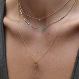 Close-up of a woman's collarbone area wearing a yellow gold Signature Cable Chain with a Gold Letter Charm in M, Confetti Necklace - Blue and a Single Diamond Layering Necklace. 
