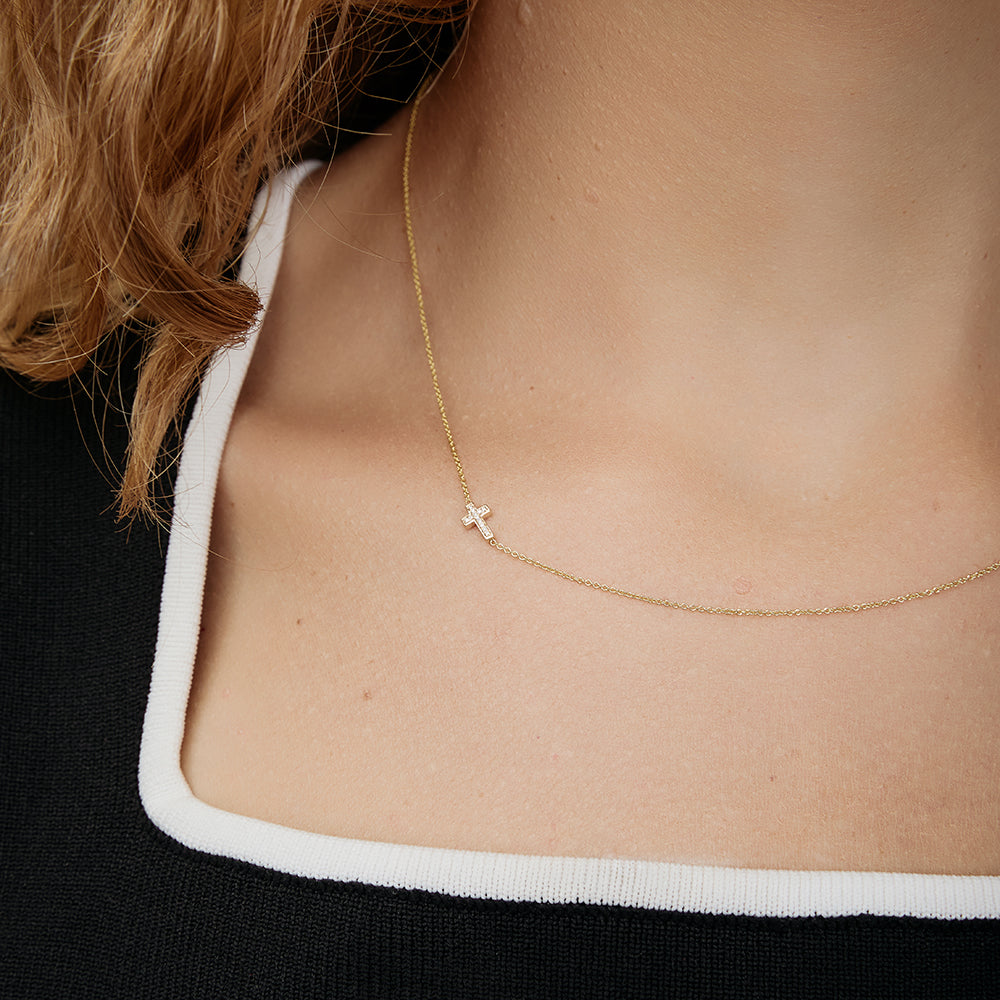 Gold necklace with a small cross charm on a person's neck
