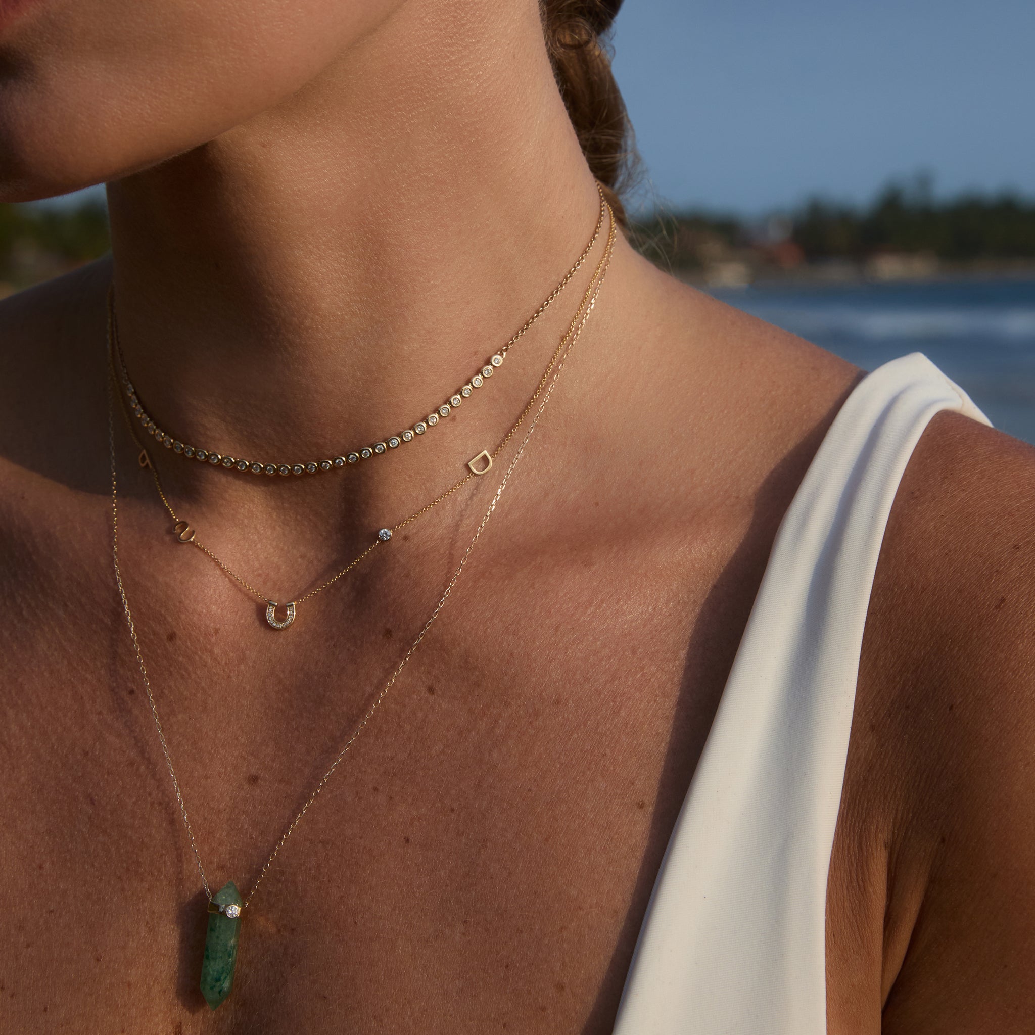 Model wearing the 5 Letter Custom Necklace layered with diamonds and an In Flow crystal pendant.