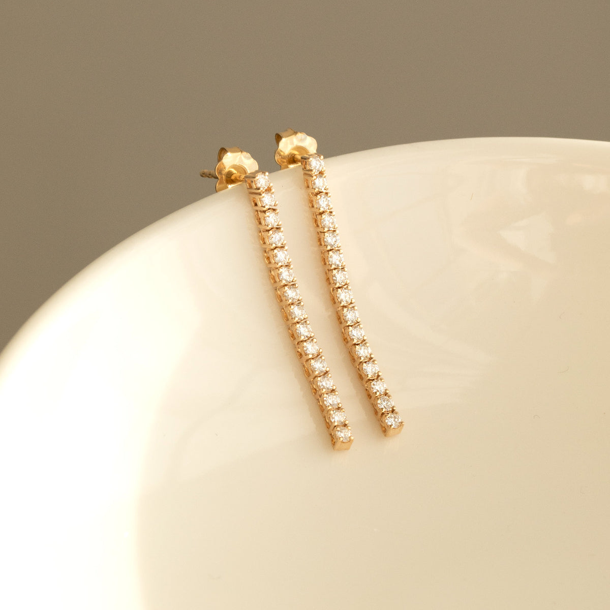 A pair of Down the Line Earrings in yellow gold laid on a white bowl against a neutral background. 