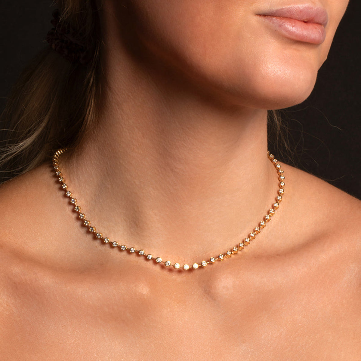 A close-up of a woman's neck wearing The Ultimate Diamond Necklace against a black background. 