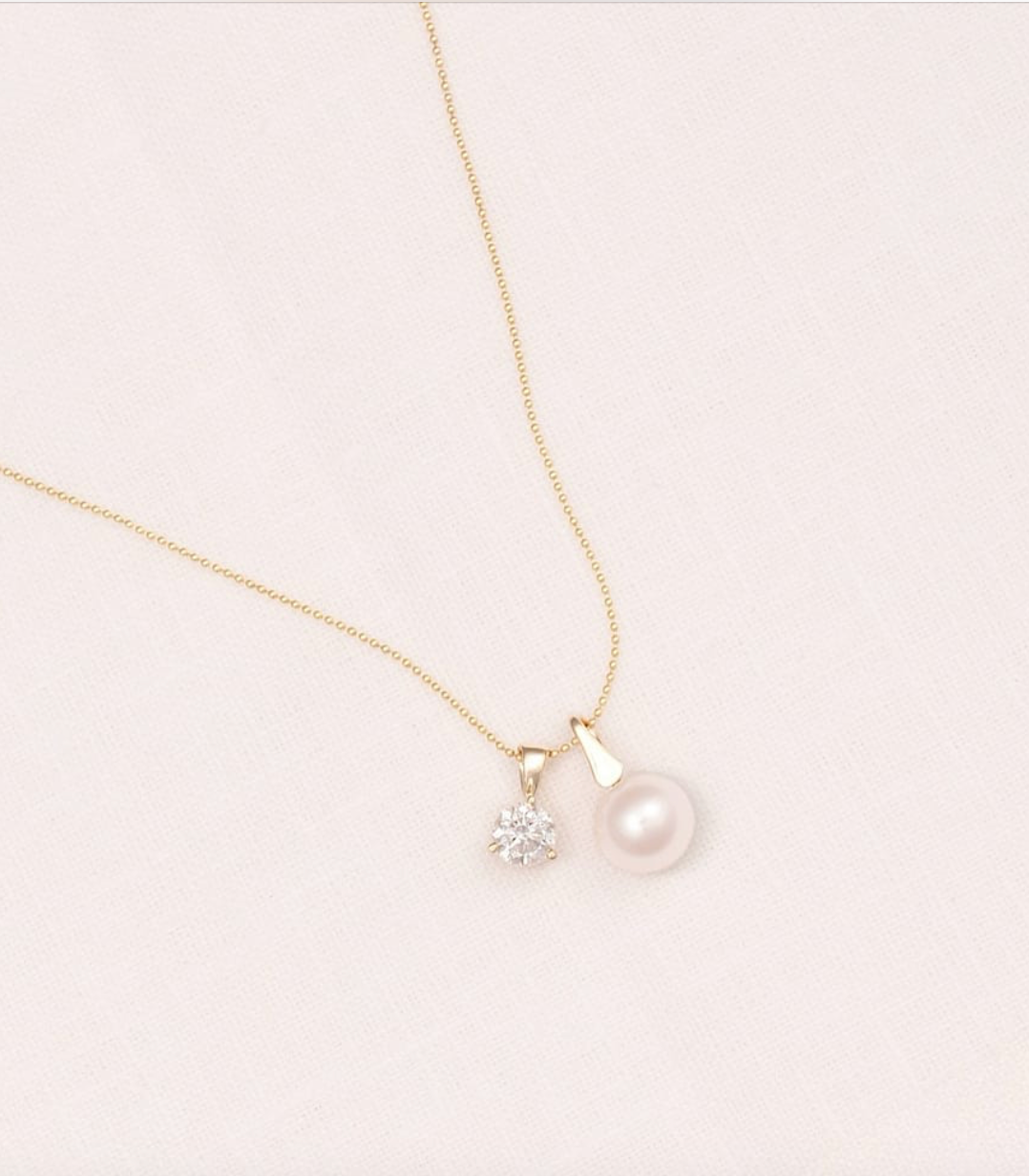 Gold necklace with a pearl and small diamond pendant on a light pink background