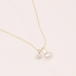 Gold necklace with a pearl and small diamond pendant on a light pink background