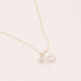 Gold necklace with a pearl and small diamond pendant on a light pink background