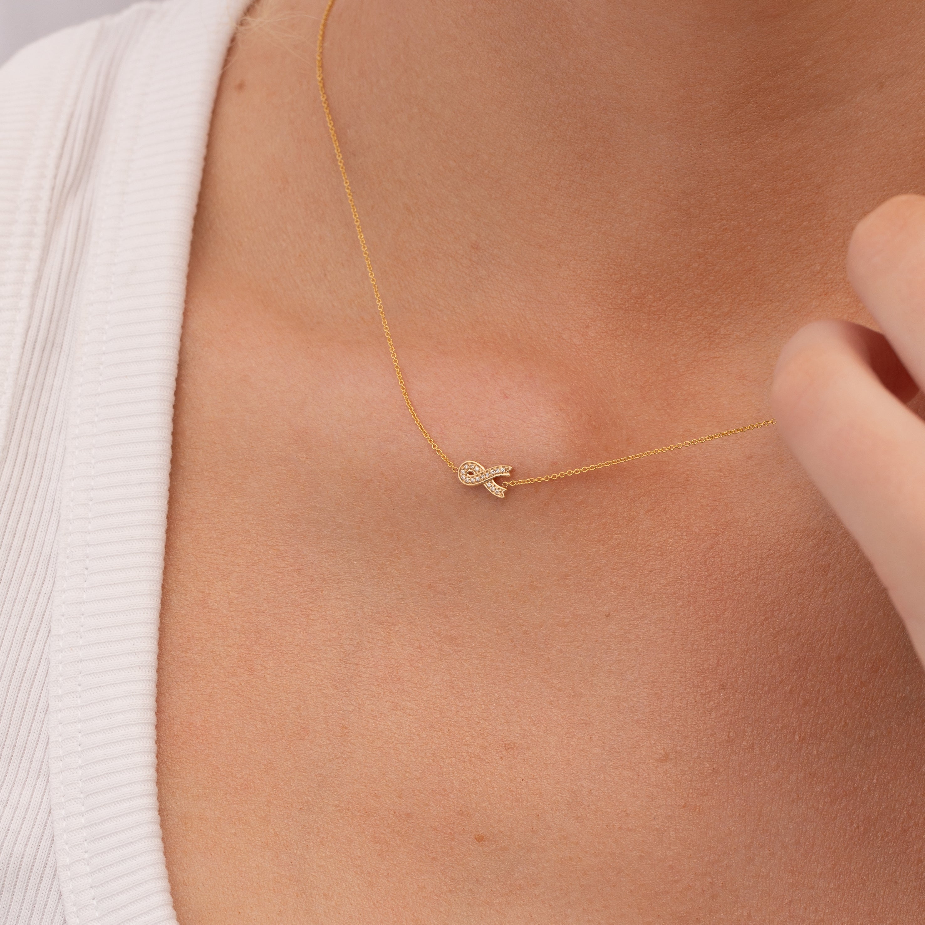Gold necklace with a small pavé diamond ribbon charm on a person's neck