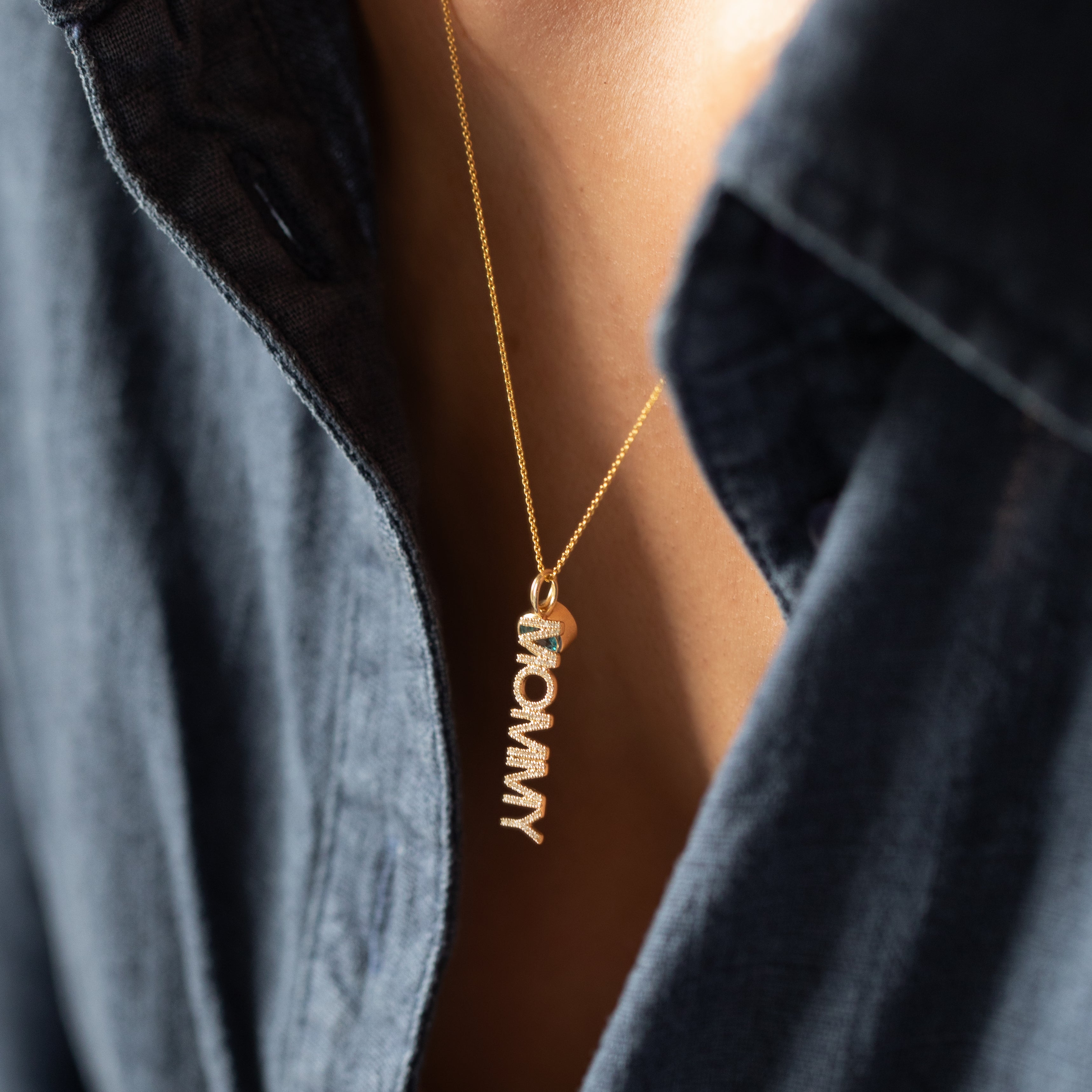 Gold necklace with a pavé diamond 'mommy' pendant on a person wearing a dark blue shirt.