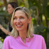 A woman wearing a Diamond Cascade Earring with blonde hair and a pink top against a green leafy blurred background.