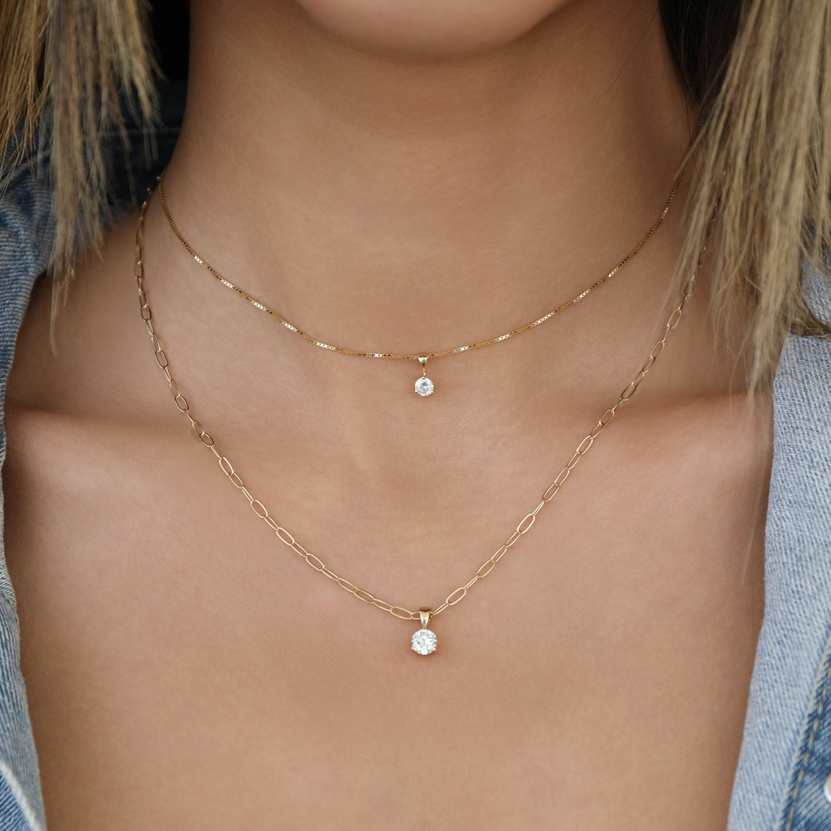 Close-up of a decellotage wearing a Duchess Diamond Pendant on The Slide Chain and a Princess Diamond Pendant on  an Element Short Link Chain, all in yellow gold. 