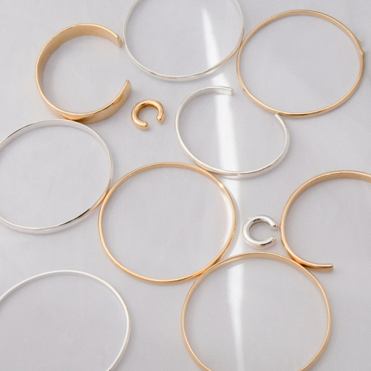 Two Ready to Mingle Ear Cuffs and several bracelets, including an All in Cuff, Plus One Cuffs, For Keeps Bangles and Flirt Bangles on a light grey surface.  