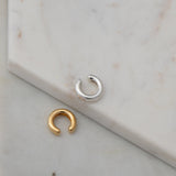 Two Ready to Mingle Ear Cuffs, one in sterling silver and the other in gold vermeil on a white marble surface.