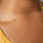 Gold necklace with a emerald gemstone on a person wearing a yellow top.