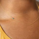 Gold necklace with a emerald gemstone on a person wearing a yellow top.