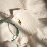 An Endless Summer Necklace - Sea + Sky and Element Short Link Chain with a Golden Spiral Shell on a white shell and white textured fabric. 