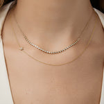 Close-up of a person wearing a diamond necklace layered with an asymmetrical star charm necklace.