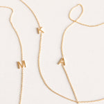 Three gold necklaces with single letter charms, being M, K and A on a plain background. 