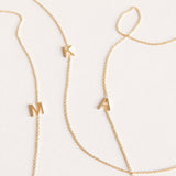 Three gold necklaces with single letter charms, being M, K and A on a plain background. 