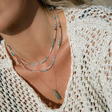 Close-up of a blonde woman’s décolletage wearing two Endless Summer Necklaces - Capri and The Inflow Retreat Necklace,  styled in a cream crochet top. 