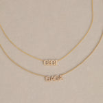 A GIGI Necklace in yellow gold with a cable chain and a Pavé Necklace in yellow gold with a bead chain, against a light beige background. 