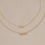 A GIGI Necklace in yellow gold with a cable chain and a Pavé Necklace in yellow gold with a bead chain, against a light beige background. 