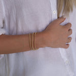 A woman’s arm wearing the Dainty Bubble Bracelet Set in yellow gold, with a white shirt.