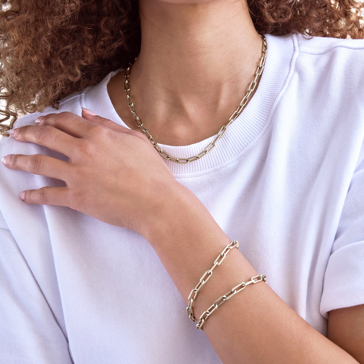 A close-up of a woman wearing a Bold Link Chain and two Bold Link Bracelets, styled with a white t-shirt.