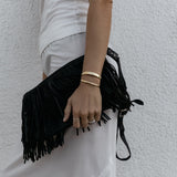 A person wearing an All in Cuff and Plus One Cuff in gold, an Etched Paris Ring in white gold, a C'est Moi Link Ring in rose gold and an Open Diamond Ring in yellow gold, styled in a white top and light grey pants against a textured white background. 