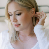 A Thin Gold Hoop, Lip Stud, Element Long Link Chain and Custom Gold Necklace – 3 Letters worn by a blonde woman with a white top, against a blurred background. 